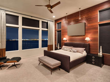 Furnished master bedroom interior in new home with amazing view of city lights and water at nightの写真素材