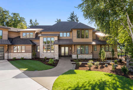 Luxury home exterior on sunny day with blue sky. Features three car garage, large driveway, and elegant designの写真素材