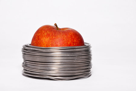 Wired apple: whole red apple in coils of aluminum wire isolated on white backgroundの写真素材