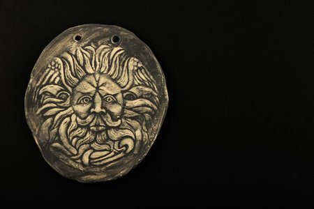 Tourist ceramic souvenir replica of male Gorgon Medusa head in Minerva temple in Roman Bath in England isolated on blackの写真素材