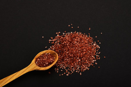 Handful of red Hawaiian sea salt with wooden spoon isolated on black paper backgroundの写真素材