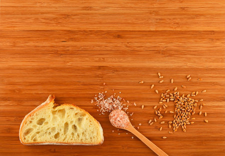 Wooden bamboo cutting board with spoon of pink Himalayan salt, handful of ripe grains and slice of...