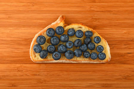 Wooden bamboo cutting board with sandwich of mellow blueberries on slice of wheat breadの写真素材