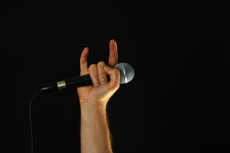 Male hand holding microphone with devil horns rock metal sign isolated on black backgroundの写真素材
