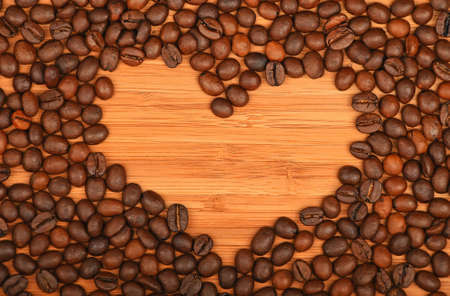Heart shaped coffee beans frame of Roasted Arabica coffee espresso beans over wooden bamboo board backgroundの写真素材