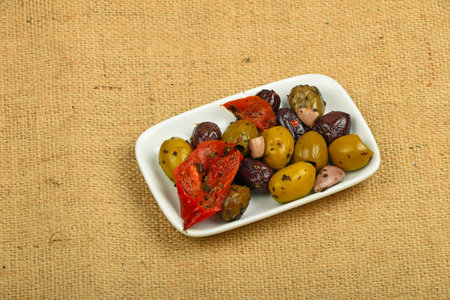 White plate of Mediterranean snack of red and green olives and pickled red pepper on burlap jute canvasの写真素材