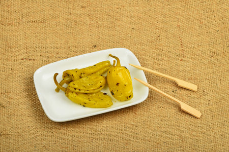 Mediterranean snack of four pickled green pepper in white plate with two skewers on burlap jute canvasの写真素材