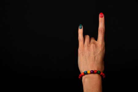 Female hand with devil horns rock metal sign symbol gesture and colorful wooden beads isolated on...