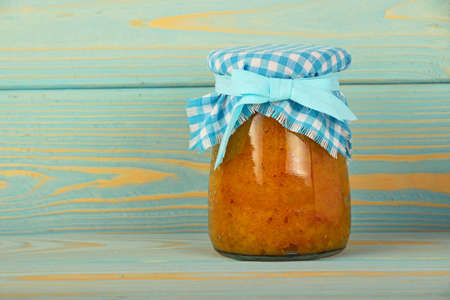 One glass jar of homemade quince jam with textile top decoration at blue painted vintage wooden surfaceの写真素材