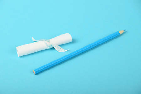 White small paper scroll note with ribbon and pencil on tender blue backgroundの写真素材