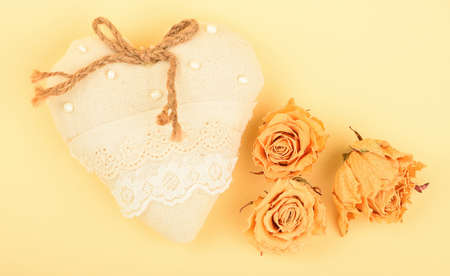 Valentine template, handmade beige toy textile lace heart with burlap jute bow, beads, dried roses and copy space on design paper backgroundの写真素材