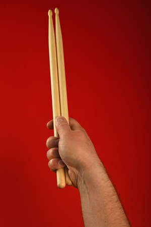 Man hand holding two wooden drumsticks over red background, point of viewの写真素材