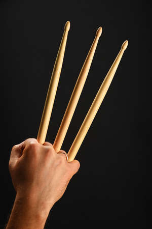 Famous wolverine claws heroic gesture, man hand holding three wooden drumsticks over black background, back view, verticalの写真素材