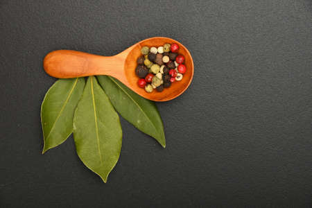 Group of three bay laurel leaves and mix of peppercorn in wooden scoop on black chalkboard backgroundの写真素材