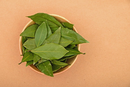 Wooden bowl of green bay laurel leaves on brown kraft paperbackground
