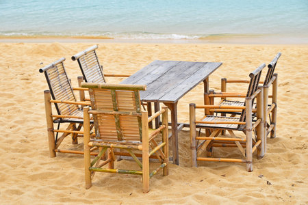Wooden bamboo furniture, table and five chairs around on san beach with blue sea water background