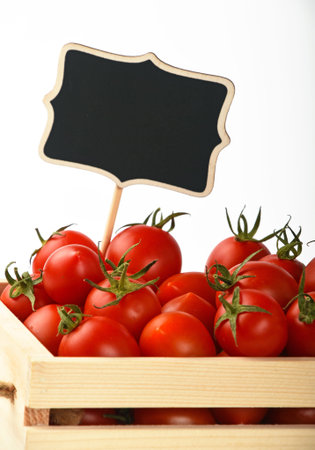 Fresh red ripe cherry tomatoes in small wooden box with black chalkboard price sign tag over white backgroundの写真素材