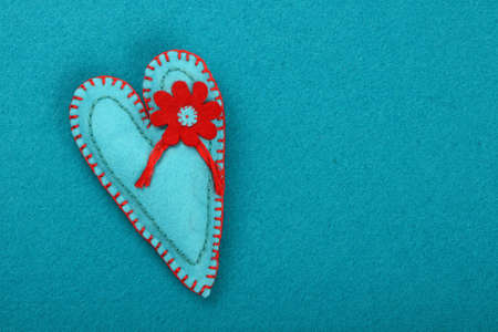 Felt craft and art, one handmade teal stitched toy heart with red flower on blue background, top viewの写真素材