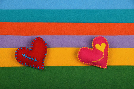 Craft and art, two handmade stitched toy hearts, pink and red on colorful felt stripes background