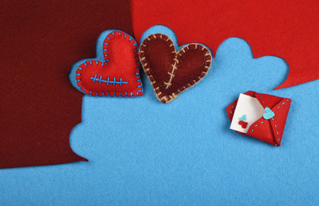 Felt craft and art, two handmade stitched toy hearts, brown and red cut out on blue felt background, with letter envelopeの写真素材