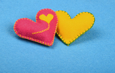 Felt craft and art, two handmade stitched toy hearts, pink and yellow together on blue background