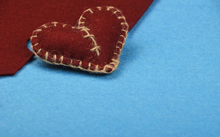 Felt craft and art, one handmade brown stitched toy heart with cut out on blue felt background, top viewの写真素材