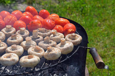 Vegetables in salt and spices being cooked outside on round summer grill, white champignons portobello mushrooms and red small tomatoesの写真素材