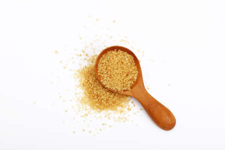 Wooden scoop spoon of brown cane sugar with pinch of sugar spilled around isolated on white background, top viewの写真素材