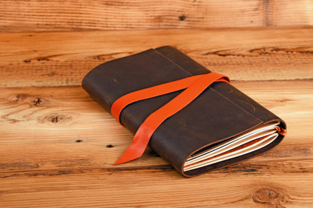 Handmade paper diary notebook in brown leather cover with orange bookmark over old vintage wooden...
