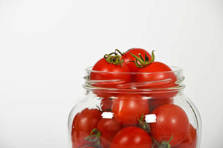 Glass jar full of red cherry tomatoes ready for conservation over white background, side viewの写真素材