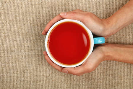 Two woman hands holding embracing big blue cup of black red over linen canvas background, warming handsの写真素材