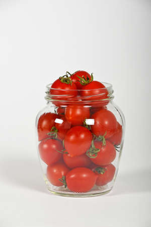 Glass jar full of red cherry tomatoes ready to pickle for conservation over white background, side viewの写真素材