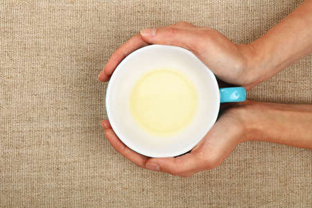 Two woman hands holding embracing big empty finished blue cup of clear green tea over linen canvas background, warming handsの写真素材