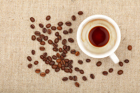 One empty finished white cup of espresso or americano and roasted coffee beans on background of...