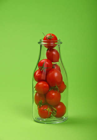 Big glass bottle full of red cherry tomatoes over green background as symbol of fresh natural organic juice or ketchupの写真素材