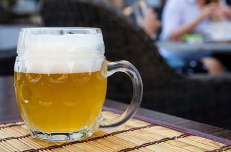 One glass mug of unfiltered craft draft white wheat weizen beer on wooden bamboo mat on table, close...