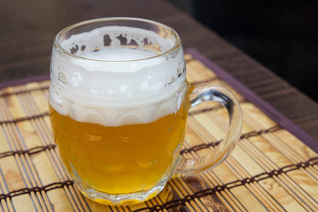 One glass mug of unfiltered craft draft white wheat weizen beer on wooden bamboo mat on table, close...