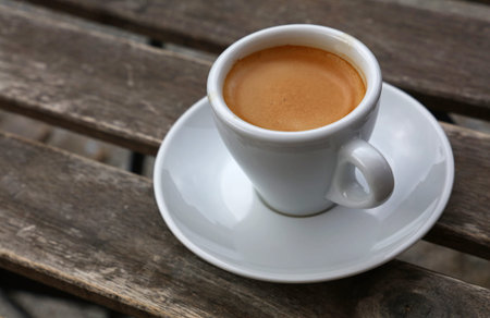 Espresso coffee shot brown crema froth in porcelain white cup with saucer over vintage wooden table,...
