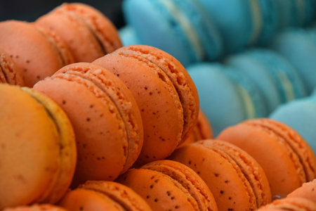 Fresh baked orange and blue macaroon pastry cookies (macarons, macaroni) in retail store display, close up, low angle viewの写真素材