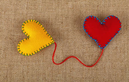 Felt craft and art, two handmade stitched toy hearts, yellow and red, connected with twine thread on canvas background, close up, elevated high angle viewの写真素材