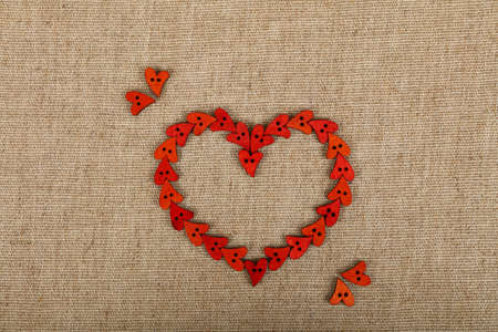Red heart shaped handmade wooden sewing buttons on linen canvas, elevated top view, close upの写真素材