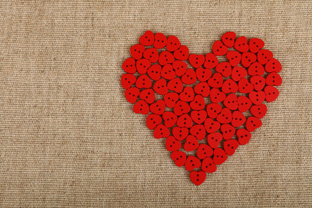 Red heart shaped handmade wooden sewing buttons on linen canvas with copy space left, elevated top...