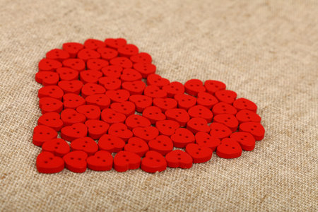 Red heart shaped handmade wooden sewing buttons on linen canvas, low angle view, close up