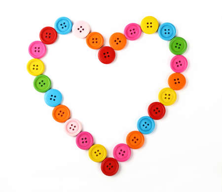 Heart shaped frame of colorful multicolor round painted wooden handmade sewing buttons isolated on white, close up, elevated top viewの写真素材