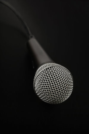 Black and silver vocal microphone with cable high angle view close up in dark, over black background, personal perspectiveの写真素材