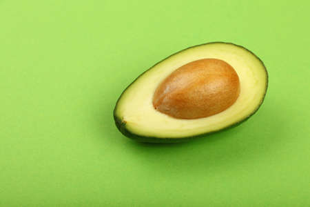 One fresh ripe avocado (Persea gratissima) half with pit stone on green paper background, detail, close up, elevated top view, high angle viewの写真素材