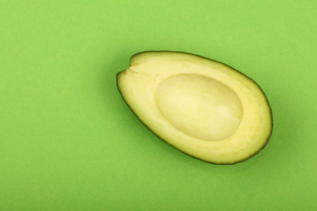 One fresh ripe avocado (Persea gratissima) half without pit stone on green paper background, detail,...