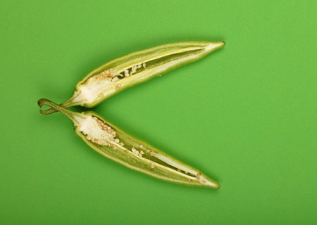 Two cut crossed halves of fresh jalapeno hot chili pepper on green paper background, close up,...