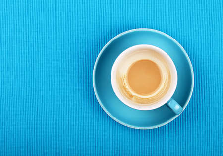 Empty cup of latte cappuccino coffee with milk on bottom, at saucer over blue tablecloth, close up, elevated top viewの写真素材