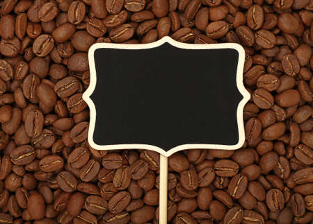 Blank black chalkboard wooden sign over background of roasted brown Arabica coffee big beans pattern, close up, elevated top viewの写真素材
